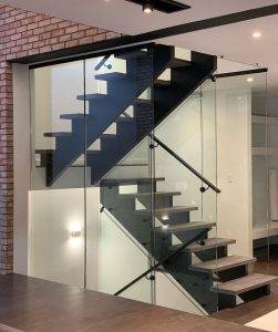 An interior view of a modern home's staircase with glass railings, floating wooden steps, and dynamic circular light fixtures against a white backdrop.
